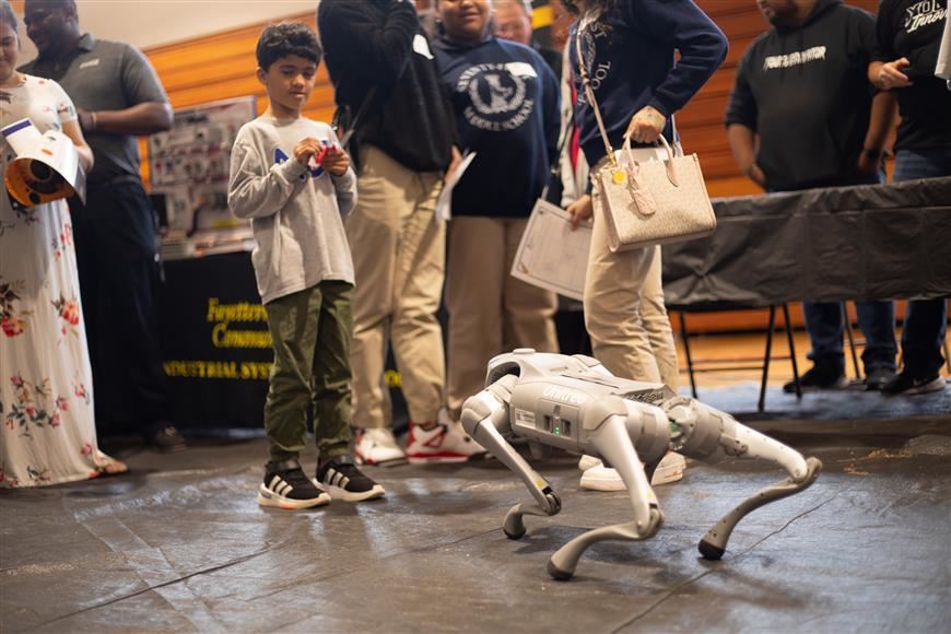 Expo attendee stops and observes robotic dog walking across the floor.